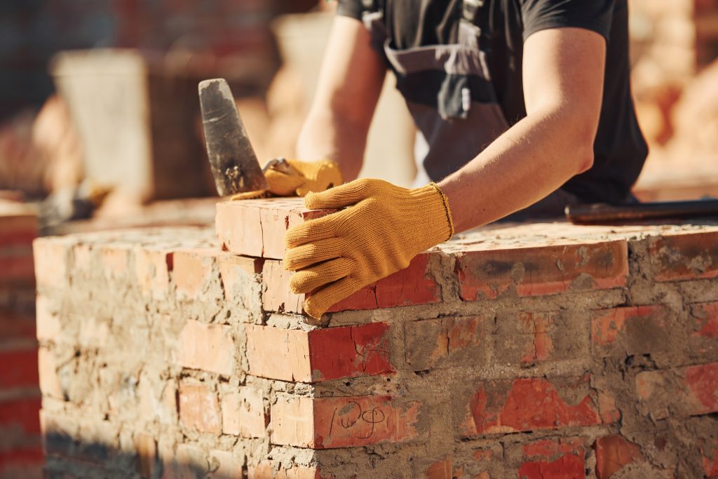 A mason contractor wearing a uniform and safety equipment is laying bricks.